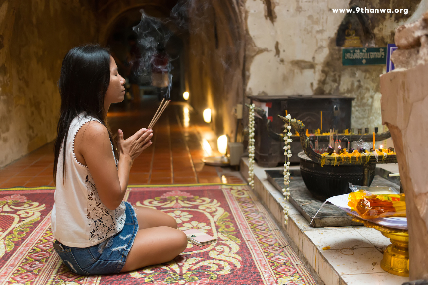 Visitors offering incense and candles at a Thai temple, symbolizing spiritual connection and respect